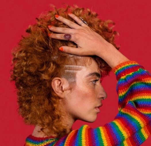 Large image of girl with red hair, rainbow sweater on red background