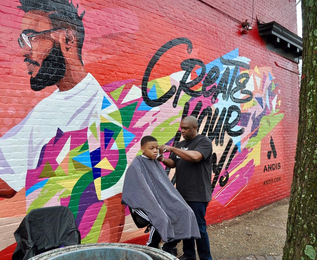 Brighter Community Atlanta barber cutting child hair in front of the wall mural